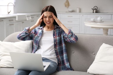 Photo of Young woman with laptop suffering from migraine at home