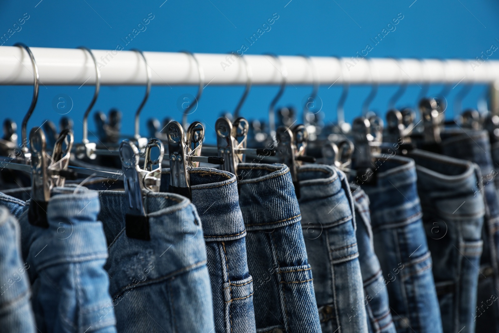 Photo of Rack with stylish jeans on blue background, closeup