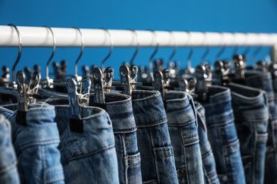 Rack with stylish jeans on blue background, closeup