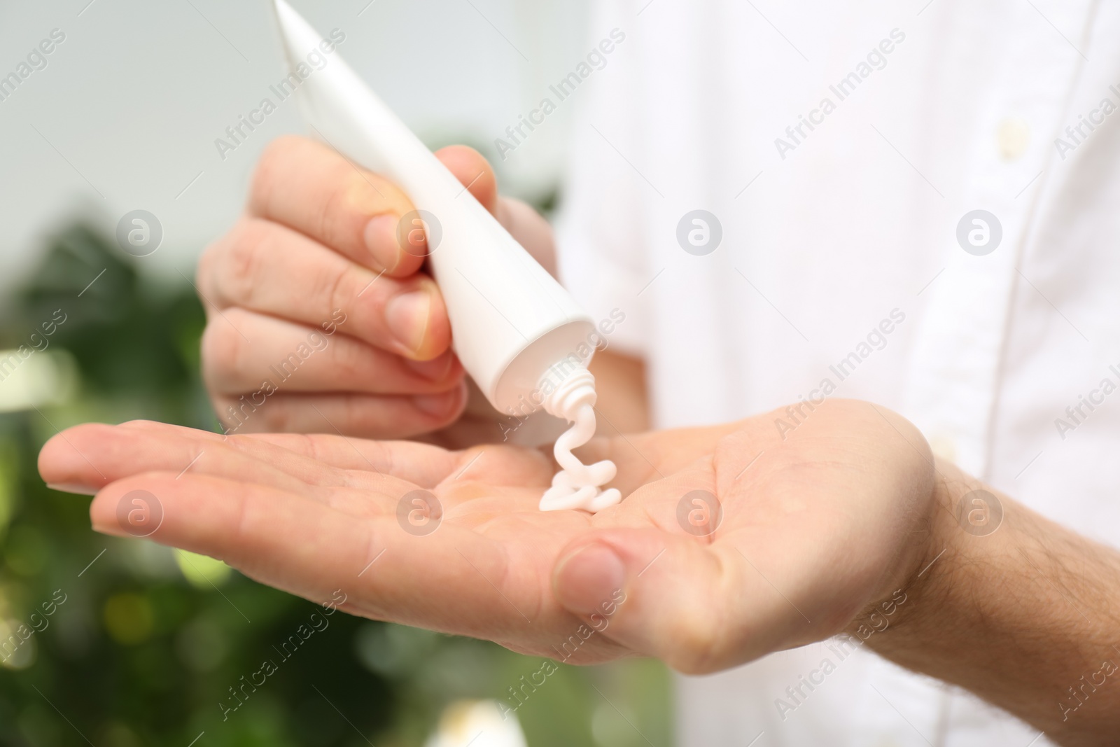 Photo of Man applying moisturizing cream from tube onto hand on blurred background, closeup