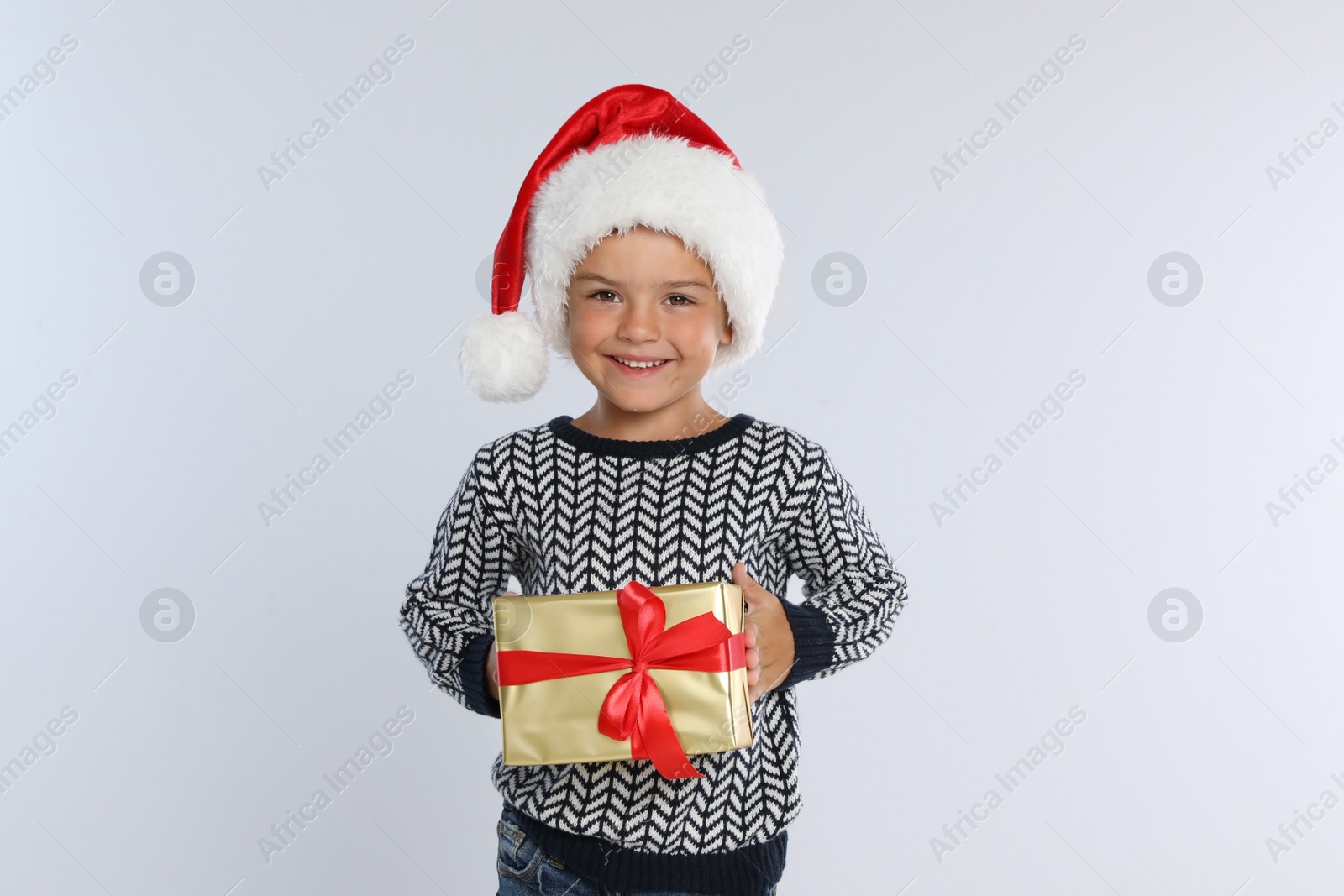 Photo of Happy little child in Santa hat with gift box on light grey background. Christmas celebration