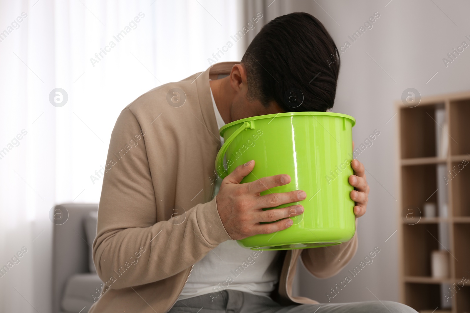 Photo of Man with bucket suffering from nausea at home. Food poisoning