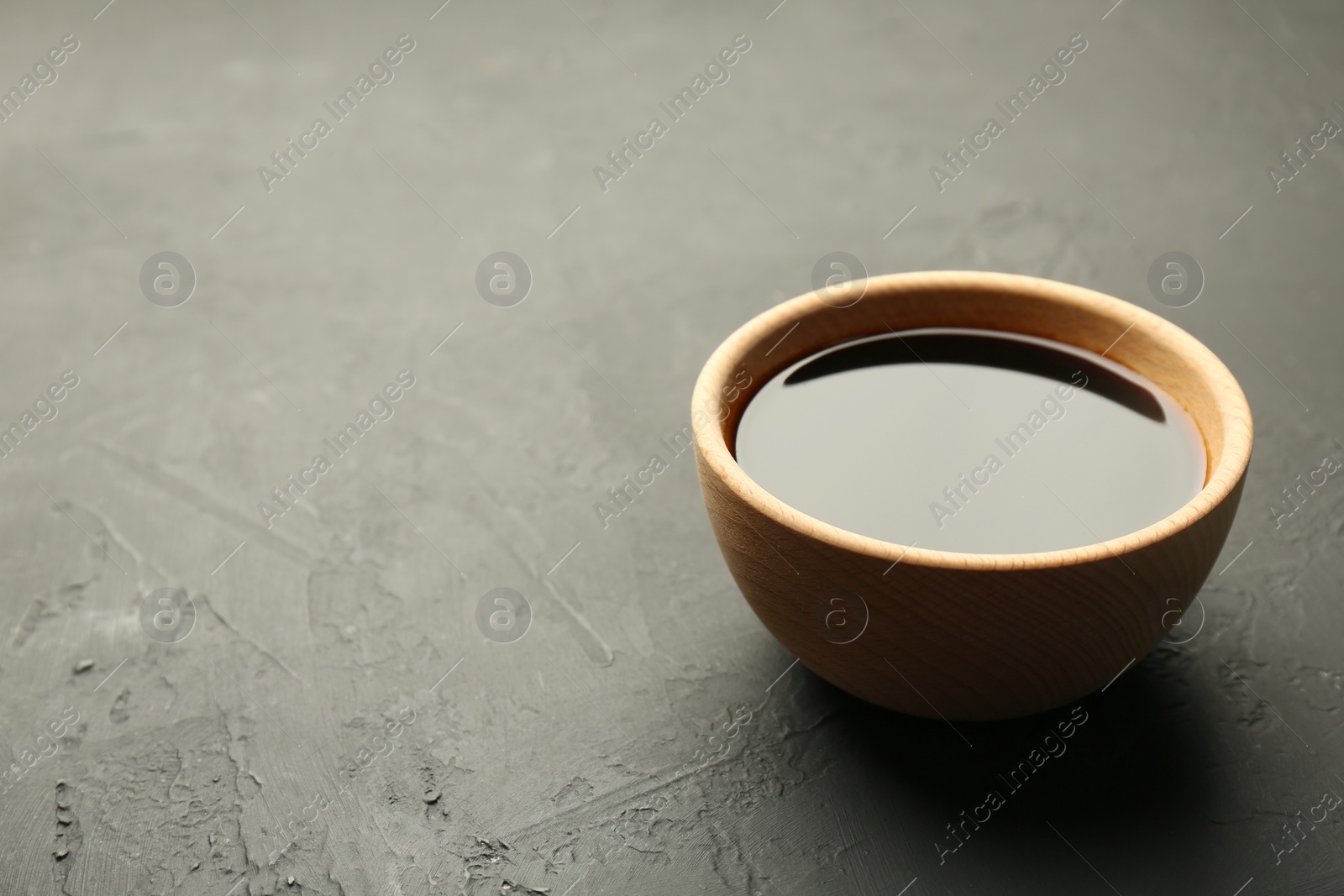 Photo of Soy sauce in wooden bowl on black textured table. Space for text