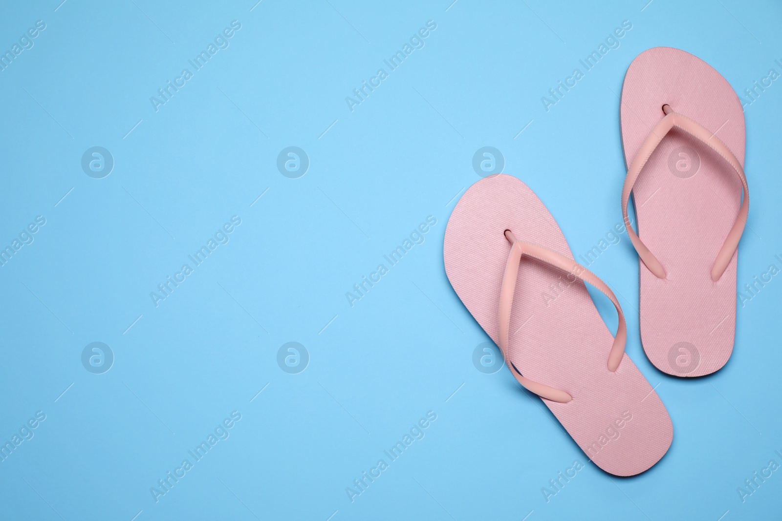 Photo of Flip flops on light blue background, top view with space for text. Beach objects