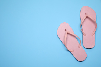 Photo of Flip flops on light blue background, top view with space for text. Beach objects