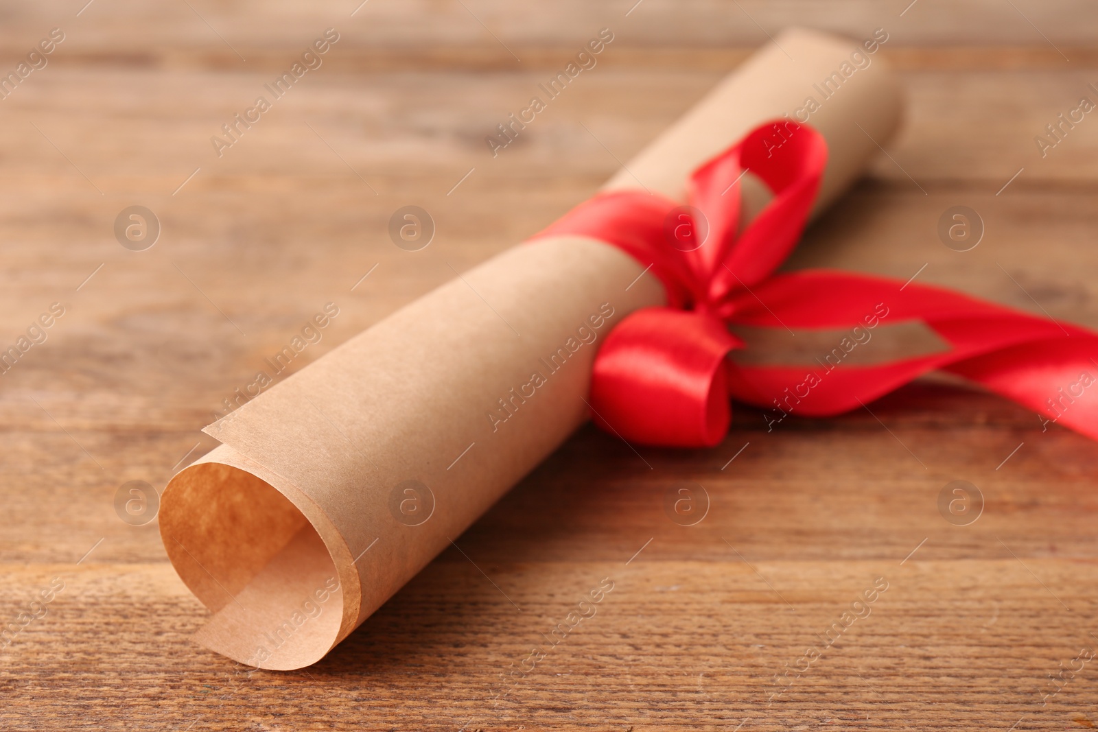 Photo of Rolled student's diploma with red ribbon on wooden table, closeup