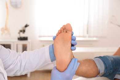 Photo of Male orthopedist checking patient's foot in clinic, closeup