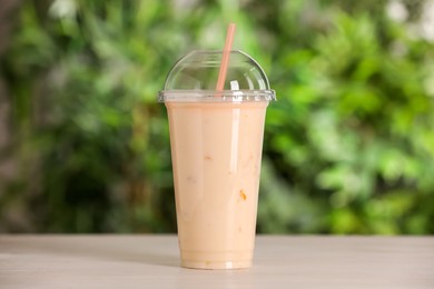 Photo of Plastic cup of tasty smoothie on wooden table outdoors