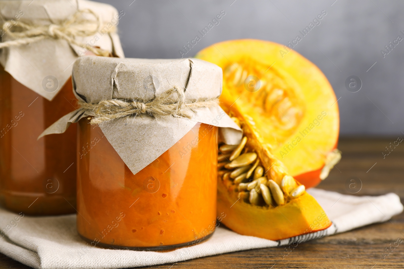 Photo of Jars of pumpkin jam and fresh pumpkins on wooden table, closeup