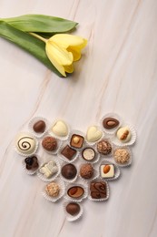 Heart made with delicious chocolate candies and beautiful tulip on beige marble table, flat lay