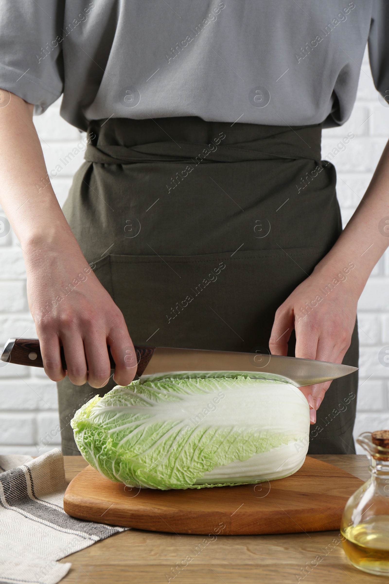 Photo of Woman cutting fresh Chinese cabbage at wooden table indoors, closeup