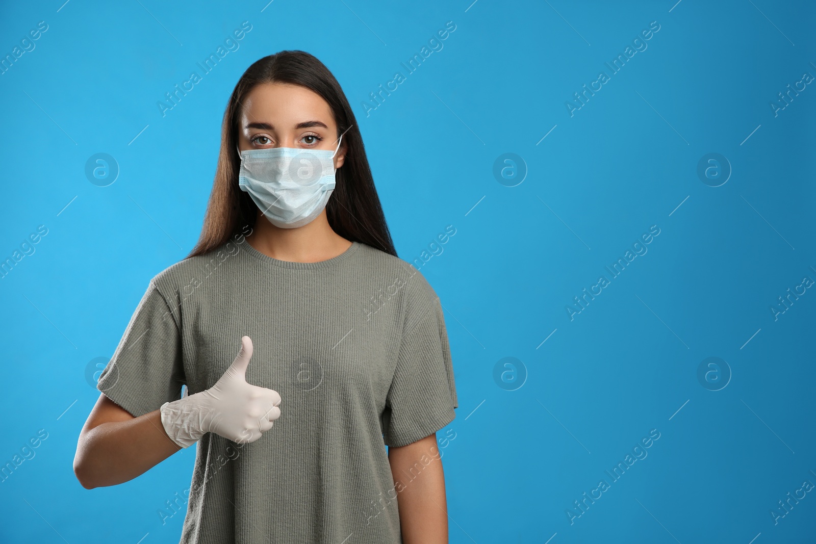 Photo of Woman in protective face mask and medical gloves showing thumb up gesture on blue background. Space for text