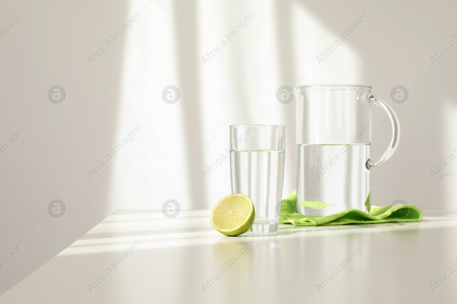 Photo of Glassware of fresh water and lime on table against light background. Space for text