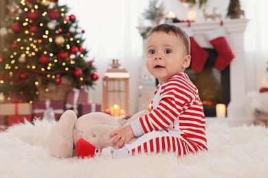 Photo of Cute baby playing with toy on floor in room decorated for Christmas