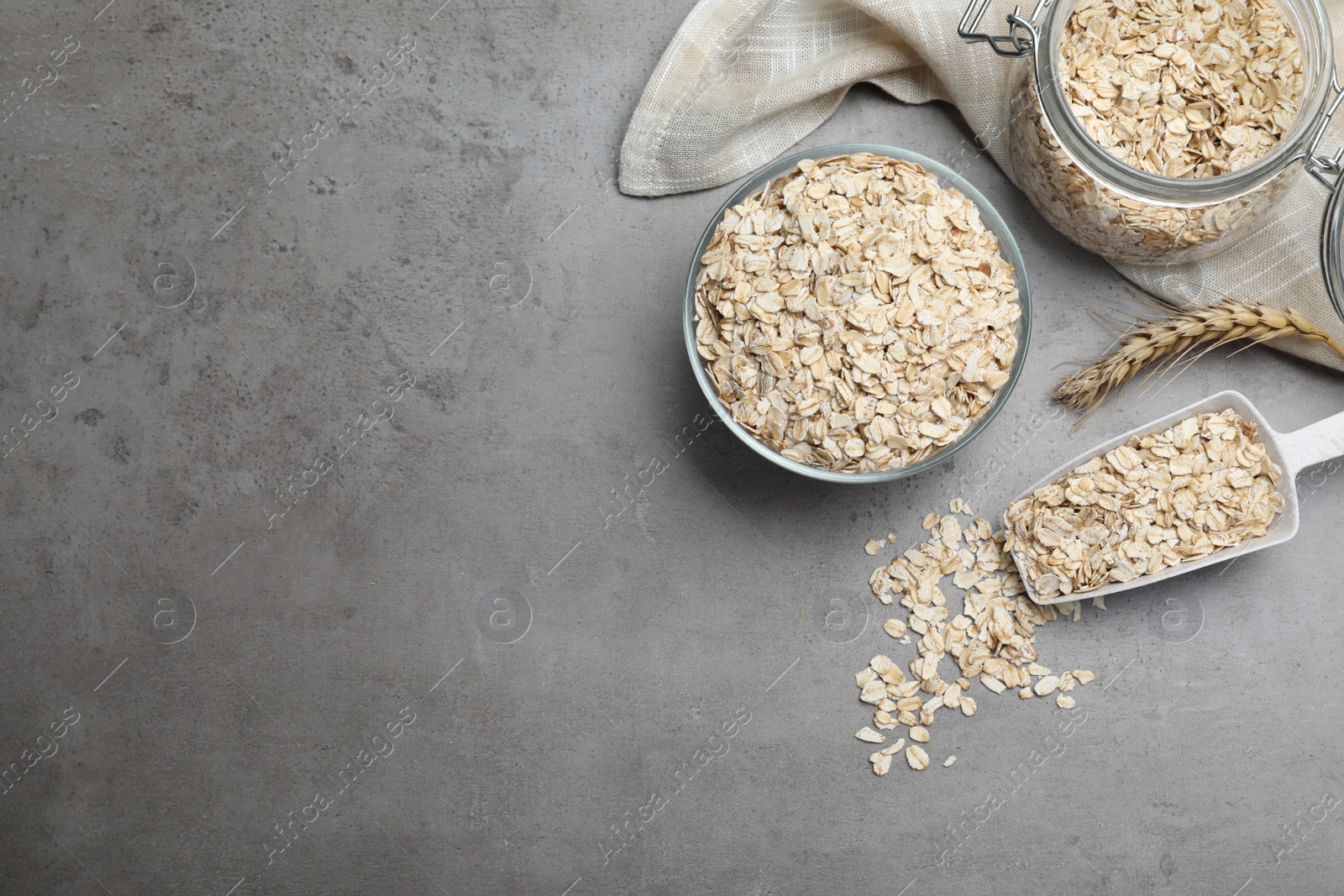 Photo of Oatmeal, glass bowl, jar and scoop on grey table, flat lay. Space for text