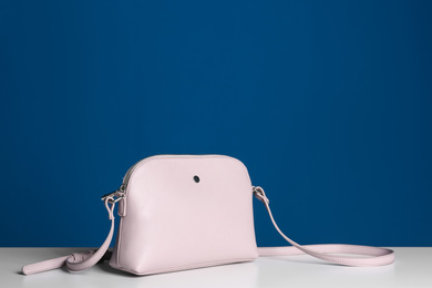 Stylish woman's bag on white table against blue background. Space for text