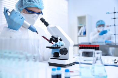 Photo of Scientist dripping sample onto glass slide while working with microscope in laboratory