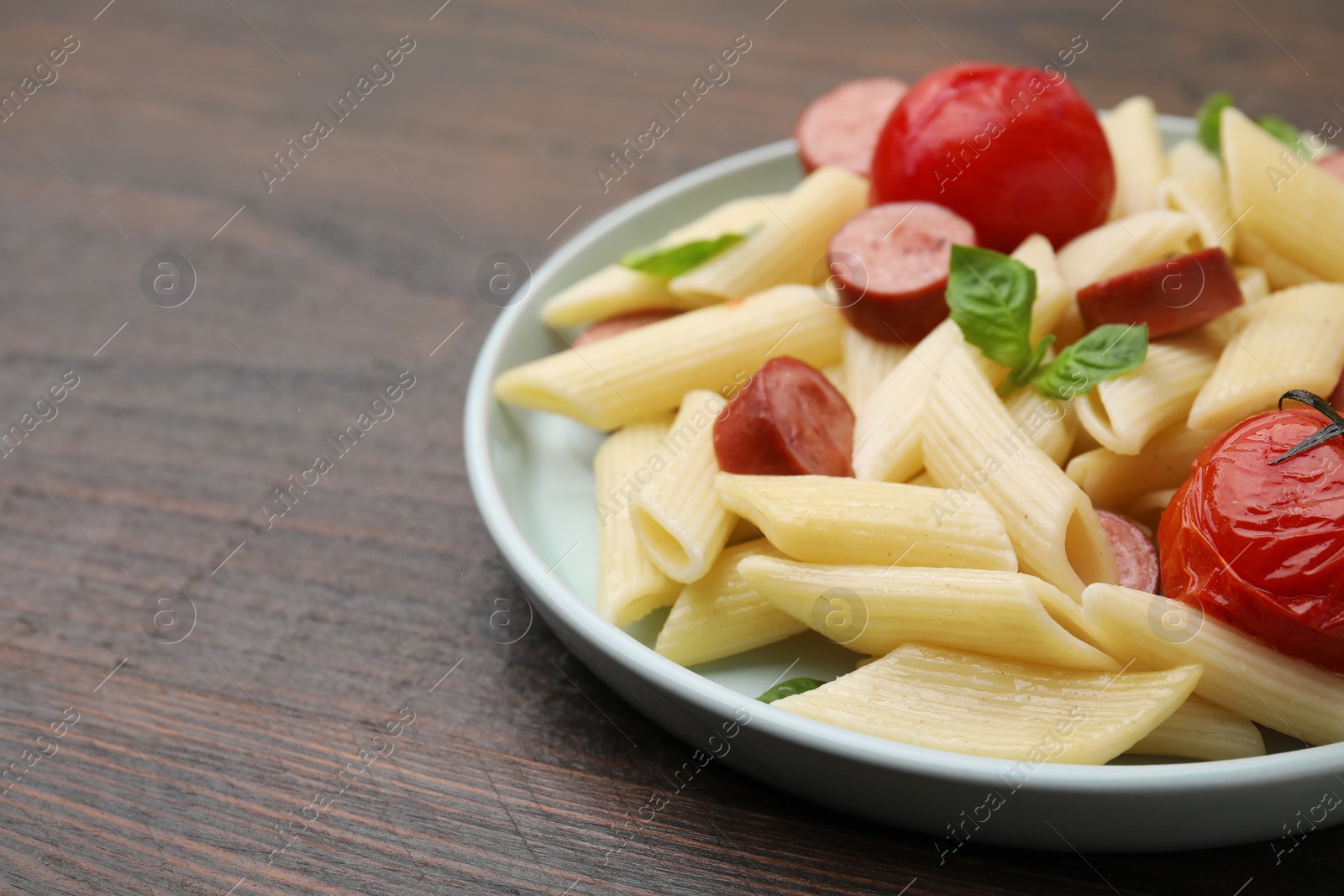 Photo of Tasty pasta with smoked sausage, tomatoes and basil on wooden table, closeup. Space for text