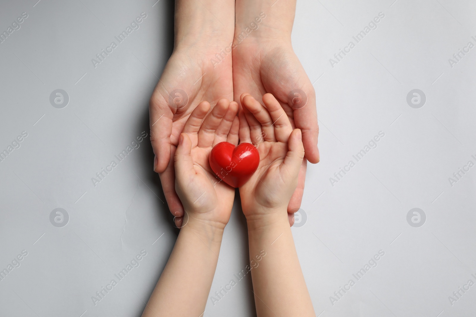 Photo of Woman and kid holding red heart in hands on light grey background, top view