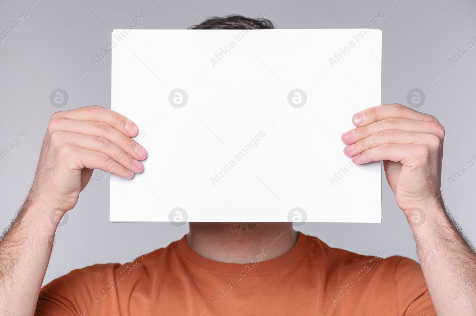 Photo of Man covering face with sheet of paper on light grey background. Mockup for design