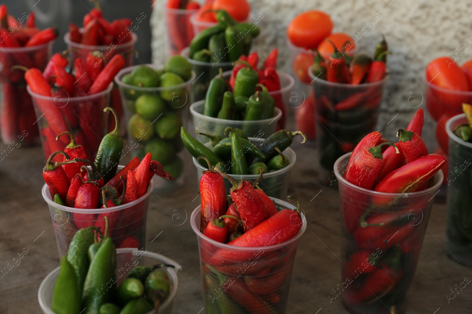 Photo of Many plastic cups with fresh chilli peppers on grey counter at market, closeup