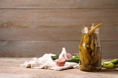 Photo of Glass jar with pickled peppers on wooden table. Space for text