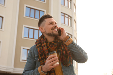 Man with cup of coffee talking on smartphone on city street in morning