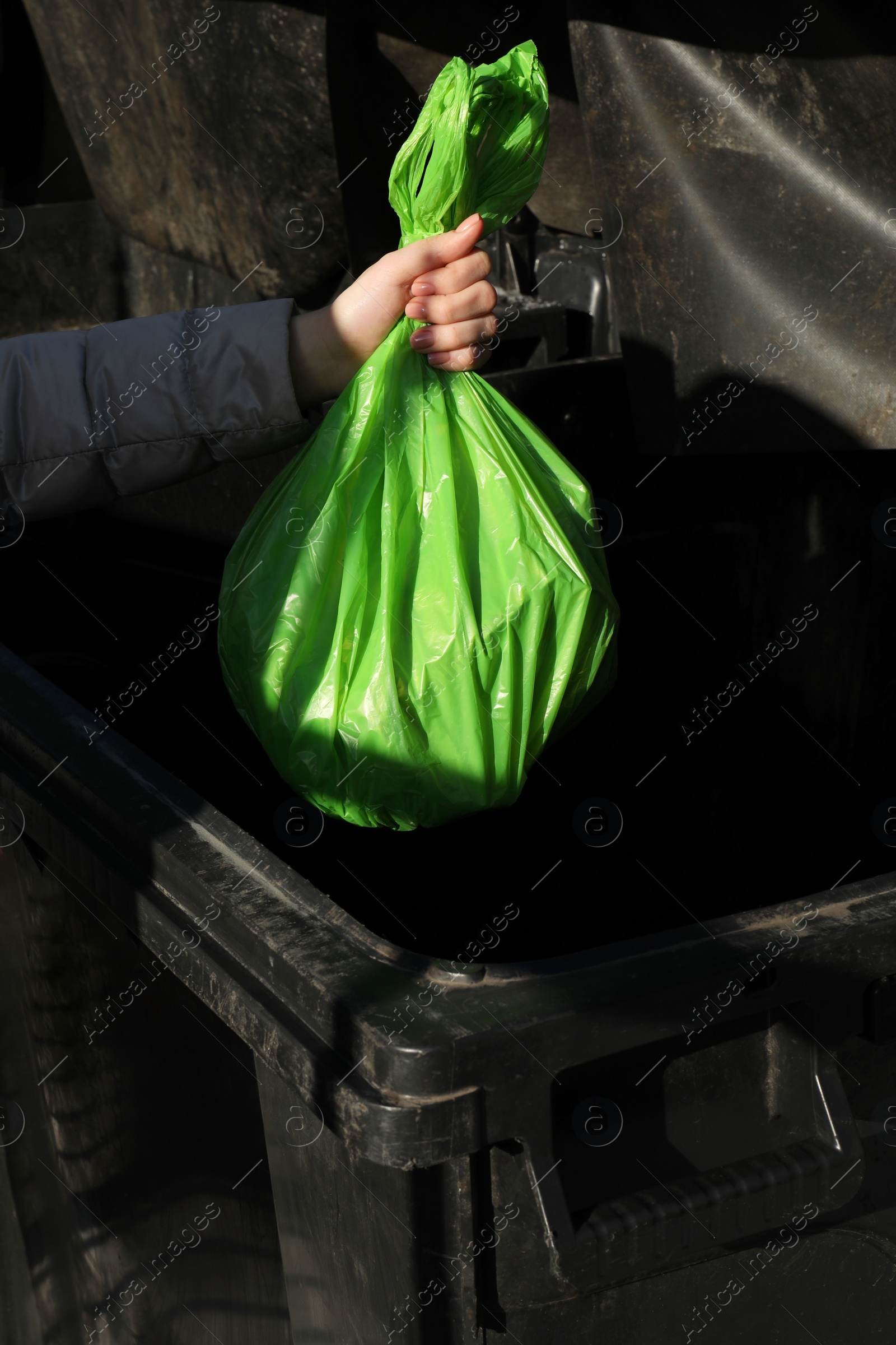 Photo of Woman throwing trash bag full of garbage in bin outdoors, closeup