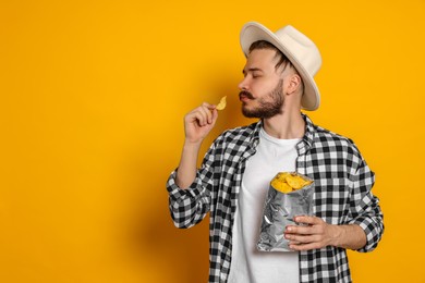 Photo of Handsome young man with bag of tasty potato chips on yellow background. Space for text