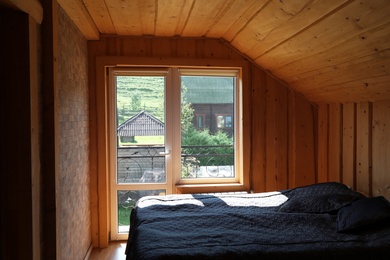 Photo of Cozy bedroom with window and wooden walls on sunny day