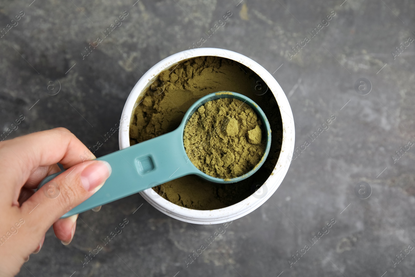 Photo of Woman taking hemp protein powder from jar at grey table, top view