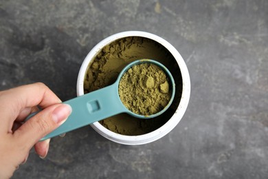 Photo of Woman taking hemp protein powder from jar at grey table, top view