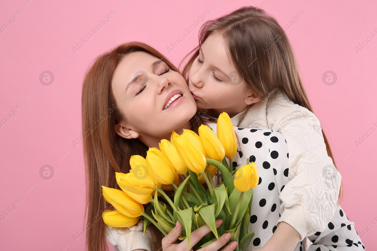 Photo of Mother and her cute daughter with bouquet of yellow tulips on pink background