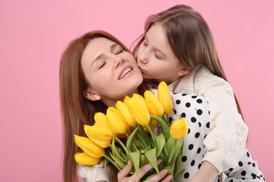Photo of Mother and her cute daughter with bouquet of yellow tulips on pink background