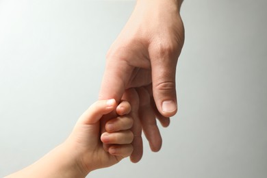 Father and child holding hands on light blue background, closeup