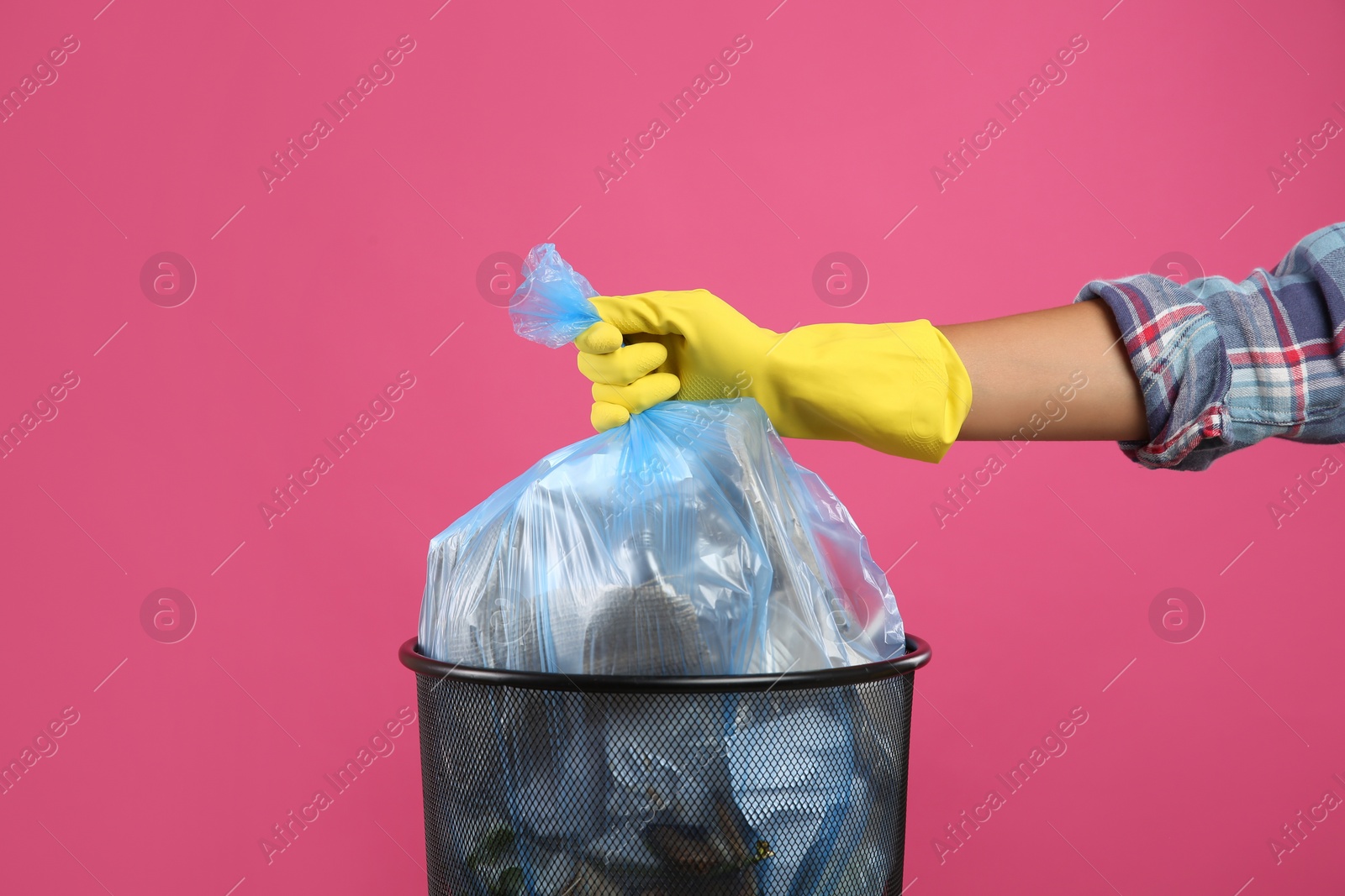 Photo of Woman taking garbage bag out of bin on pink background, closeup