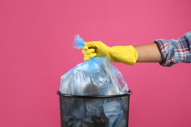 Woman taking garbage bag out of bin on pink background, closeup