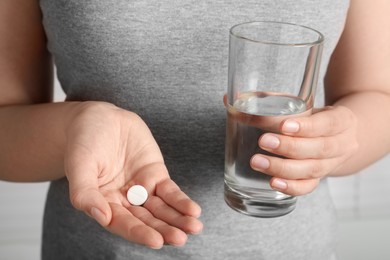 Photo of Woman holding glass of water and pill, closeup