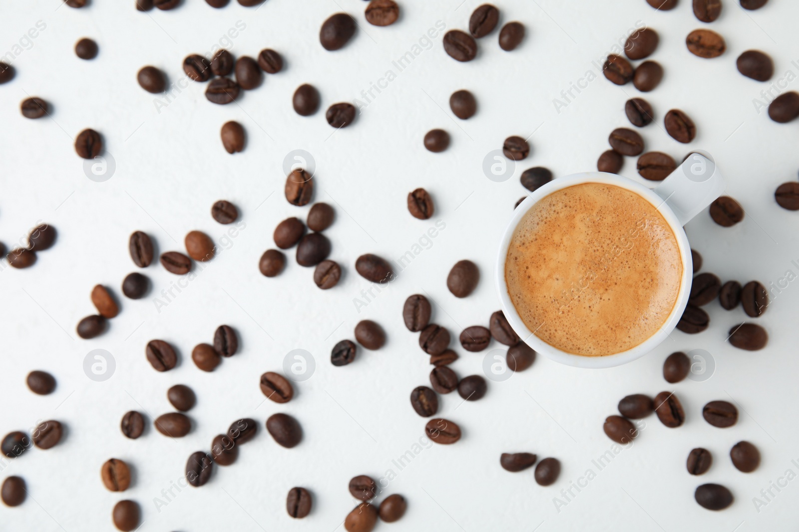 Photo of Cup of tasty espresso and scattered coffee beans on white table, flat lay