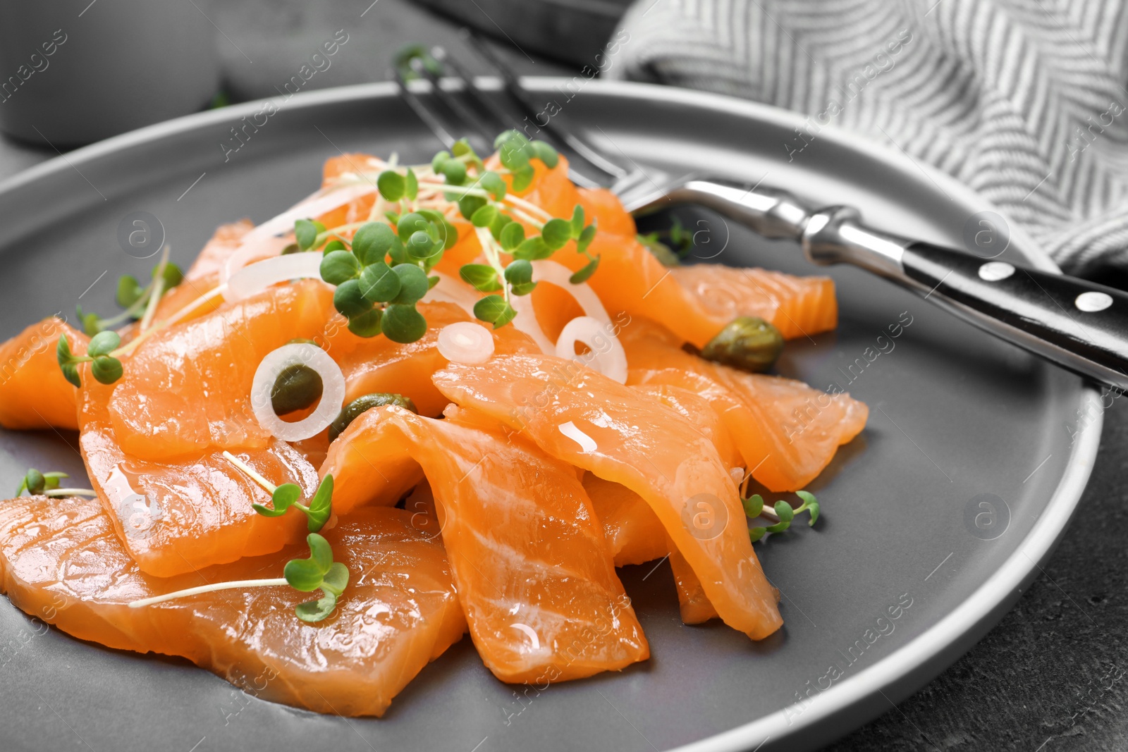 Photo of Salmon carpaccio with capers, onion and microgreens on plate, closeup