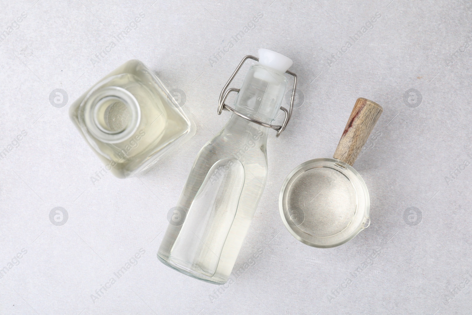 Photo of Vinegar in glass bottles and saucepan on light table, flat lay