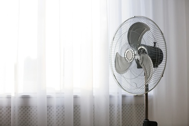 Modern electric fan near window indoors. Space for text