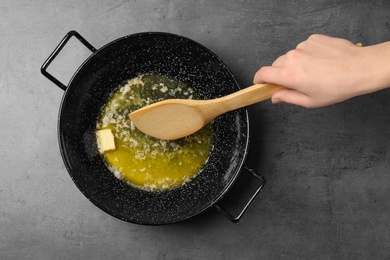 Photo of Woman mixing melting butter in frying pan on grey background, top view