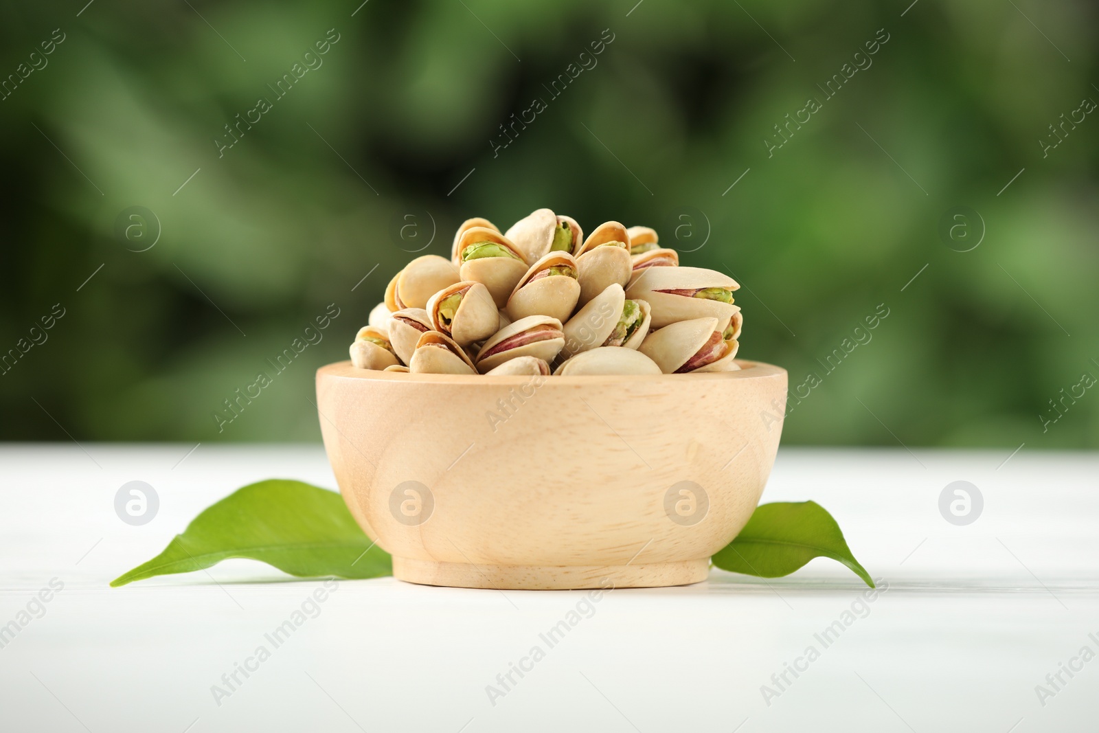 Photo of Tasty pistachios in bowl on white wooden table against blurred background, closeup