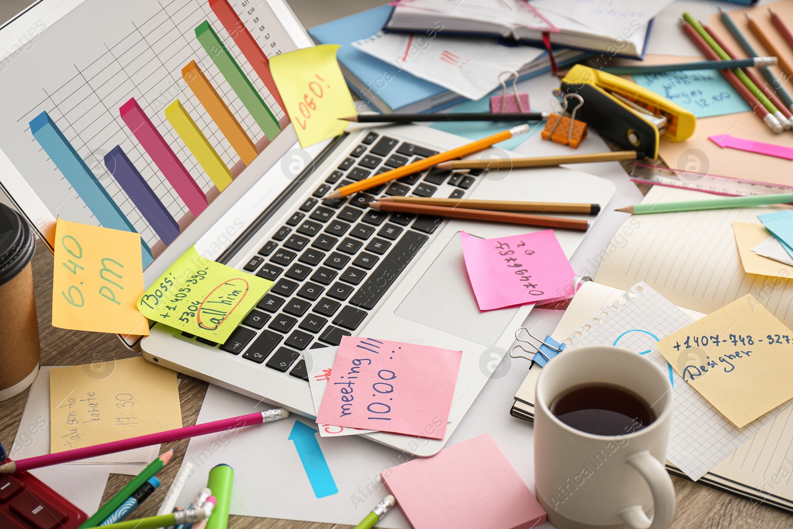 Photo of Laptop, notes and office stationery in mess on desk. Overwhelmed with work