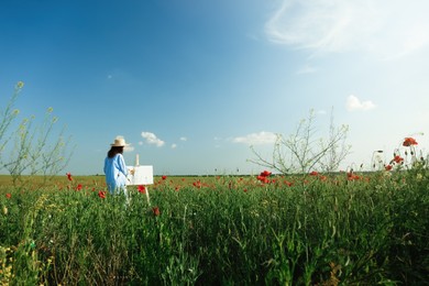 Woman painting on easel in beautiful poppy field