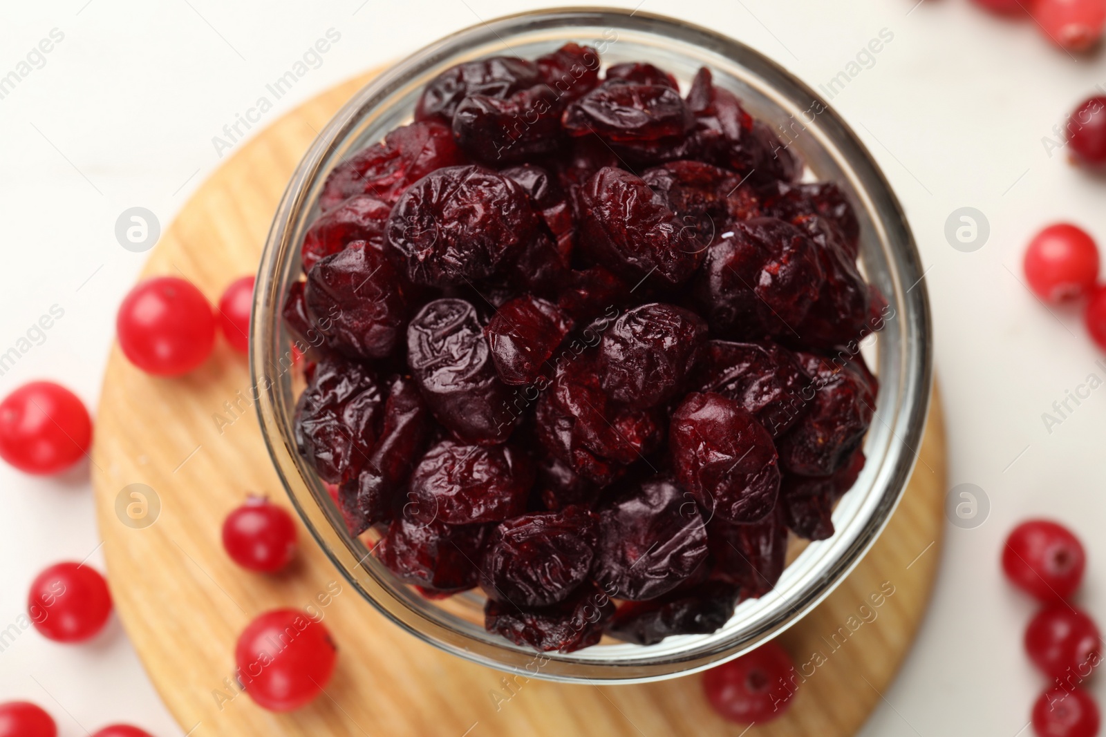 Photo of Tasty dried cranberries in bowl and fresh ones on white table, top view