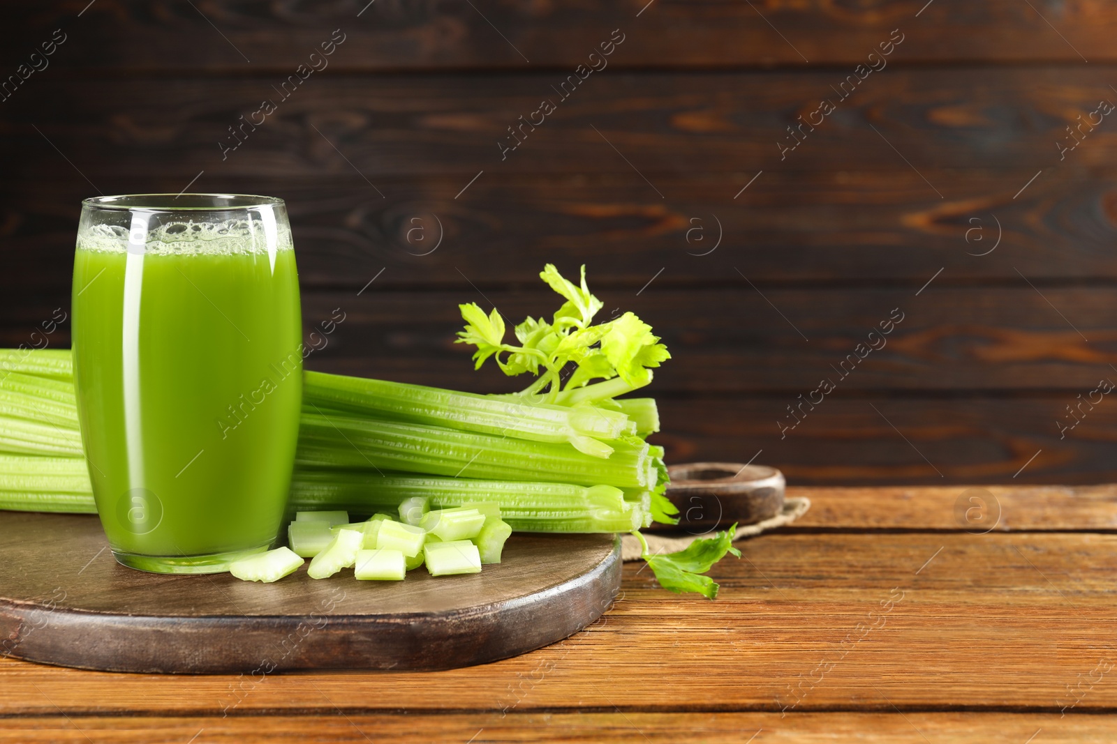 Photo of Glass of celery juice and fresh vegetables on wooden table, space for text