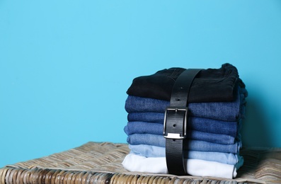 Photo of Stack of different jeans on basket against color wall with space for text