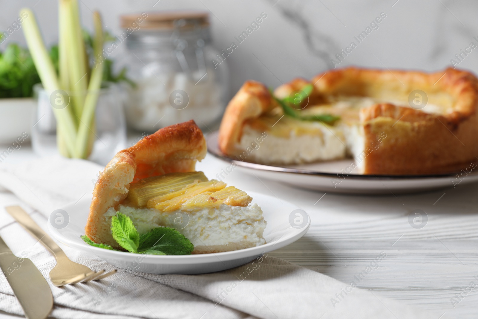 Photo of Piece of freshly baked rhubarb pie with cream cheese, mint leaves and cutlery on white wooden table